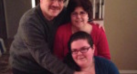 Photo of mother, daughter who is sitting in a wheelchair, and father. All with their arms around each other