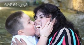 Photo of mother and son. Son is kissing mother on the cheek, the mother is smiling and hugging son