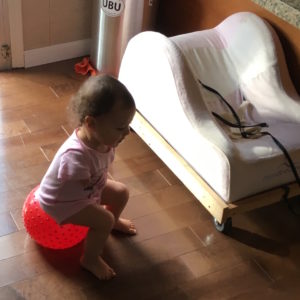 Photo of baby seat on top of dolly that has wheels underneath. Baby is sitting on a ball next to it,