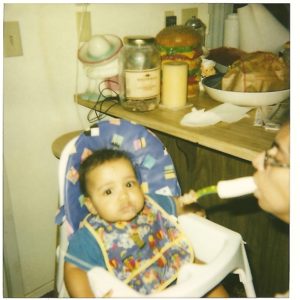 Photo shows mom spoon feeding her baby using her mouth to hold spoon.