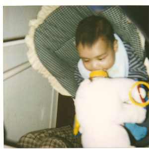 Photo of baby sitting with a bottle in mouth. The bottle is being held by a puppet.