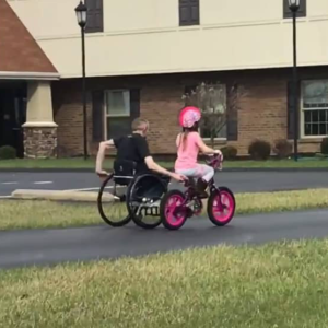 shows a father who uses a manual wheelchair and his daughter who is on a bicycle