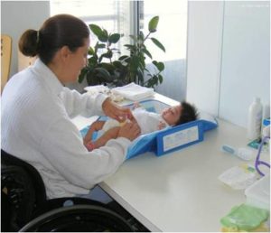 Photo of mother in wheelchair changing baby laying on a desk