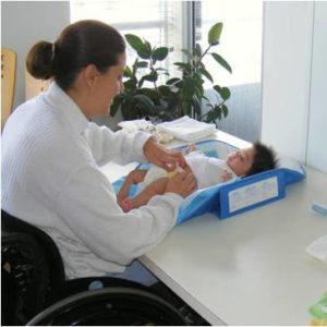 Photo of mother in wheelchair changing baby laying on a desk